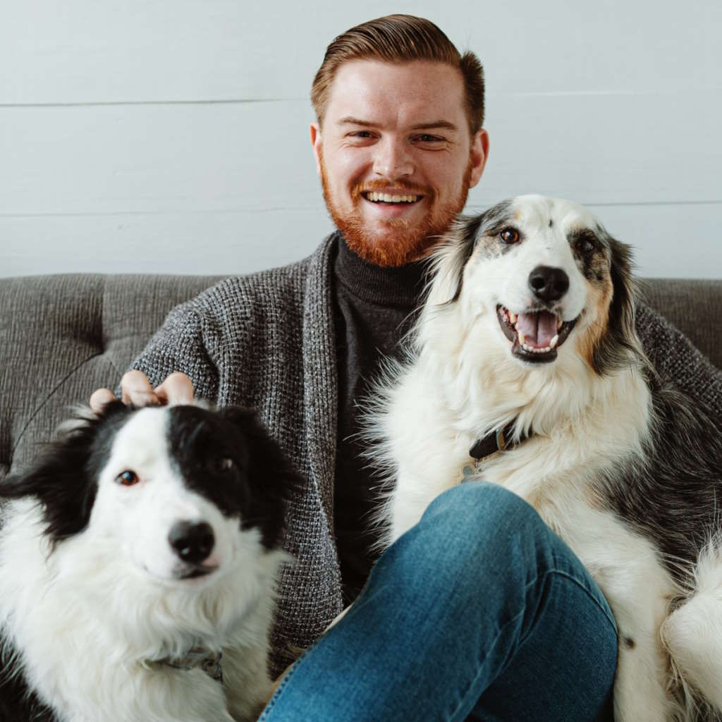 How Much Is Pet Insurance - A Man Sitting On A Couch With Two Dogs | The List Of